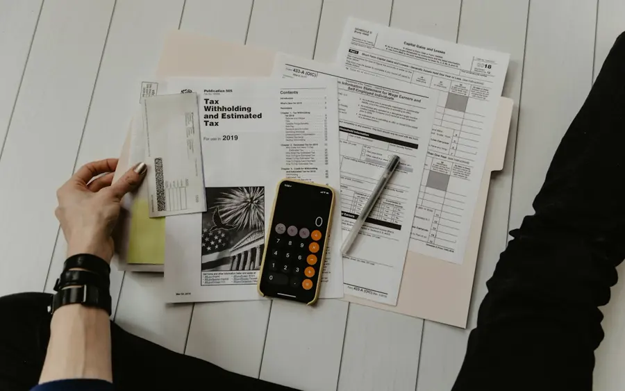 Documents de déclaration d'impôts, téléphone avec calculatrice et stylo posés au sol